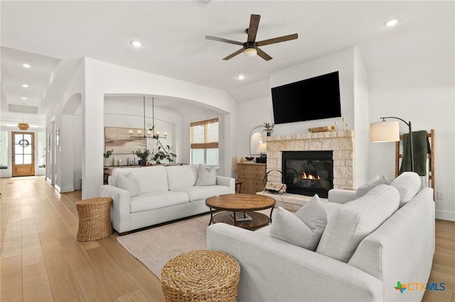 living area featuring vaulted ceiling, recessed lighting, ceiling fan with notable chandelier, a fireplace, and light wood-style floors