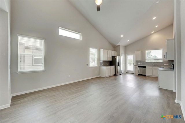 unfurnished living room with high vaulted ceiling, ceiling fan, and light wood-type flooring