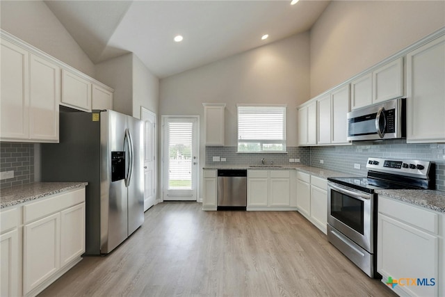 kitchen with light stone counters, decorative backsplash, white cabinetry, light wood-type flooring, and appliances with stainless steel finishes