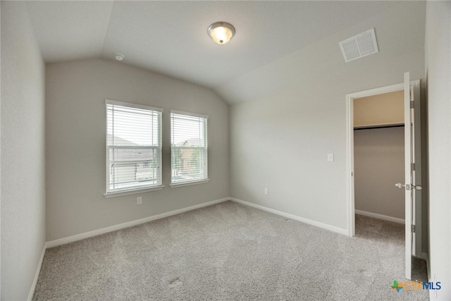 unfurnished bedroom with lofted ceiling, light carpet, a walk in closet, and a closet