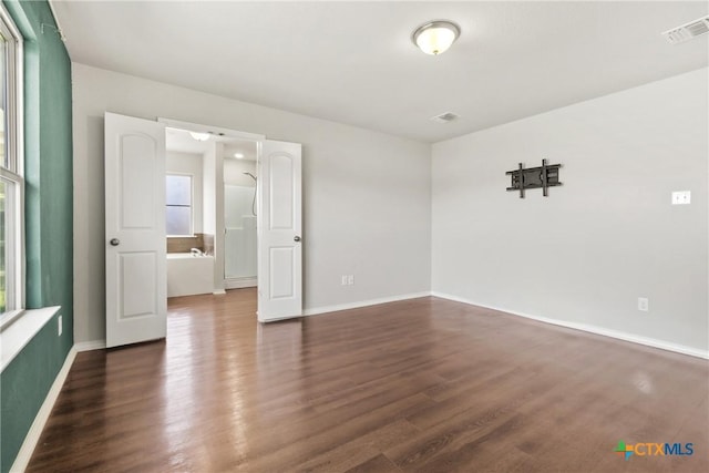 unfurnished room with dark wood-style flooring, visible vents, and baseboards