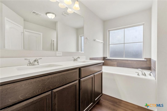 bathroom featuring a bath, double vanity, a sink, and visible vents