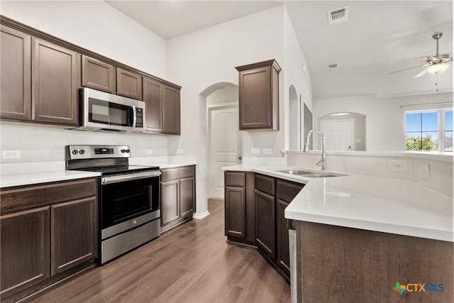 kitchen with arched walkways, appliances with stainless steel finishes, a sink, and dark brown cabinetry