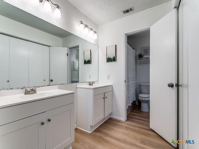 1133 Ashby St, Seguin, TX 78155 - bathroom featuring wood finished floors, two vanities, a textured ceiling, baseboards, and toilet