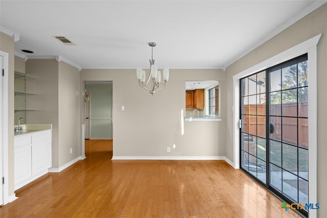 unfurnished dining area featuring crown molding, light hardwood / wood-style flooring, a chandelier, and sink