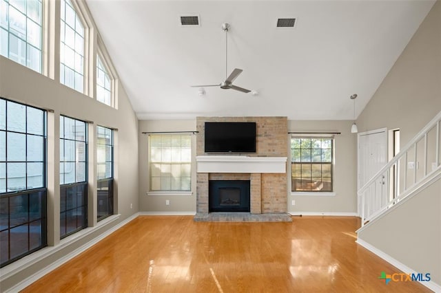 unfurnished living room with ceiling fan, high vaulted ceiling, light wood-type flooring, and a brick fireplace