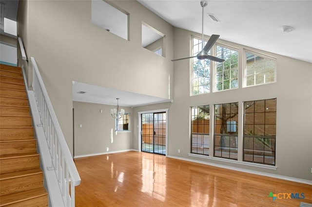 unfurnished living room featuring hardwood / wood-style floors, ceiling fan with notable chandelier, and a towering ceiling