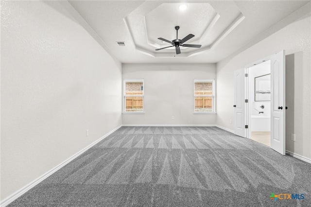 carpeted spare room featuring a tray ceiling and ceiling fan