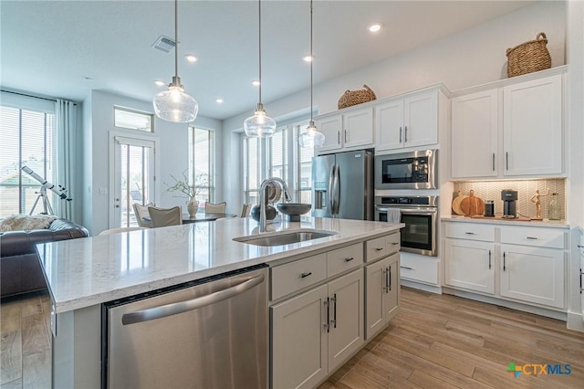 kitchen with pendant lighting, an island with sink, sink, white cabinets, and stainless steel appliances