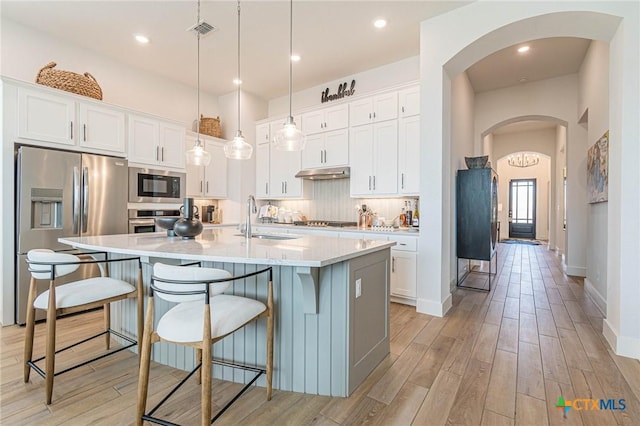 kitchen with stainless steel appliances, an island with sink, and white cabinets