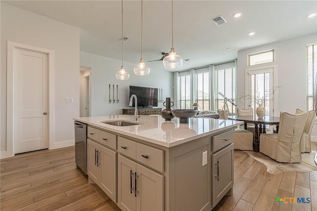 kitchen featuring sink, dishwasher, a kitchen island with sink, light stone counters, and decorative light fixtures