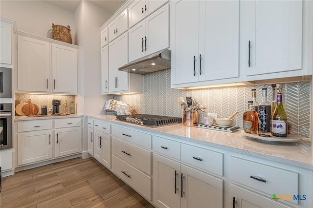 kitchen featuring appliances with stainless steel finishes, tasteful backsplash, white cabinetry, light stone counters, and light hardwood / wood-style flooring