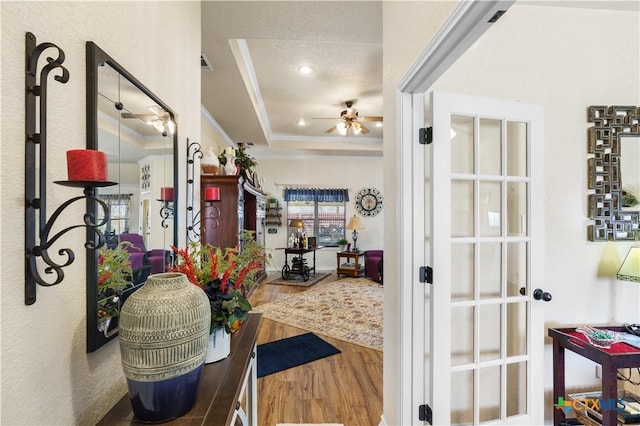 corridor with hardwood / wood-style floors, a textured ceiling, crown molding, and a tray ceiling