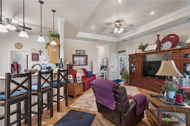 living room featuring ceiling fan, light hardwood / wood-style floors, crown molding, and a tray ceiling