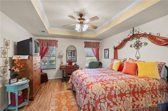 bedroom featuring ceiling fan, a raised ceiling, ornamental molding, and light wood-type flooring