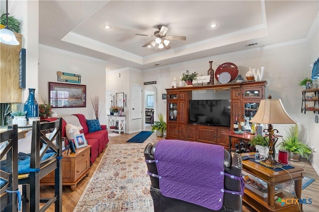 living room featuring a raised ceiling, ornamental molding, and light hardwood / wood-style flooring