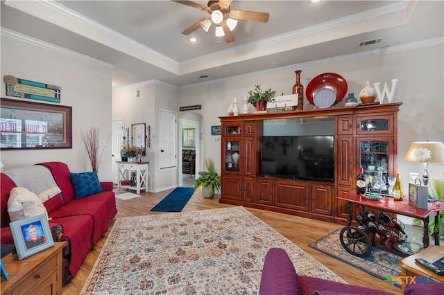 living room with a raised ceiling, crown molding, and light hardwood / wood-style flooring