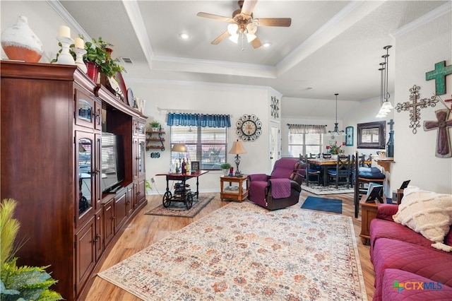 living room with a tray ceiling, ceiling fan, light hardwood / wood-style floors, and ornamental molding