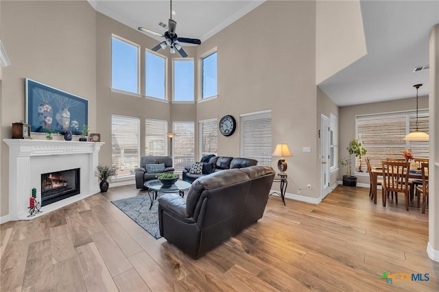 living room featuring light wood-type flooring, a fireplace with flush hearth, visible vents, crown molding, and baseboards