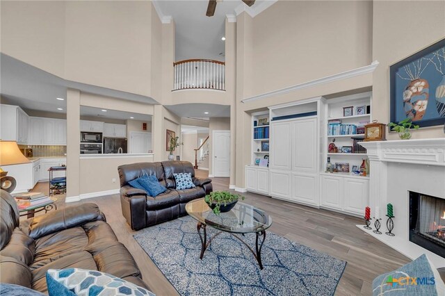 living area featuring ceiling fan, light wood-type flooring, a fireplace with flush hearth, a high ceiling, and baseboards