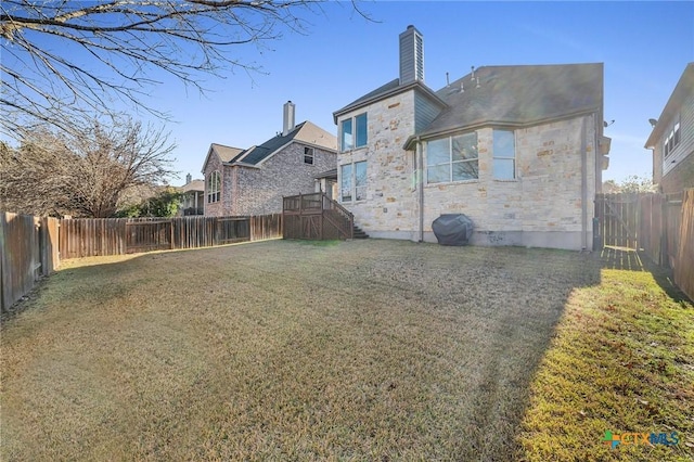 rear view of house featuring a lawn, stone siding, a fenced backyard, and a chimney