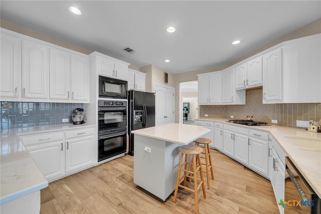 kitchen with visible vents, black appliances, light wood-style flooring, and white cabinets