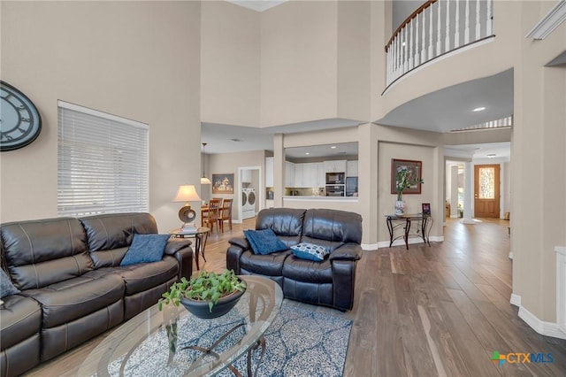 living area featuring a high ceiling, washer / clothes dryer, wood finished floors, and baseboards