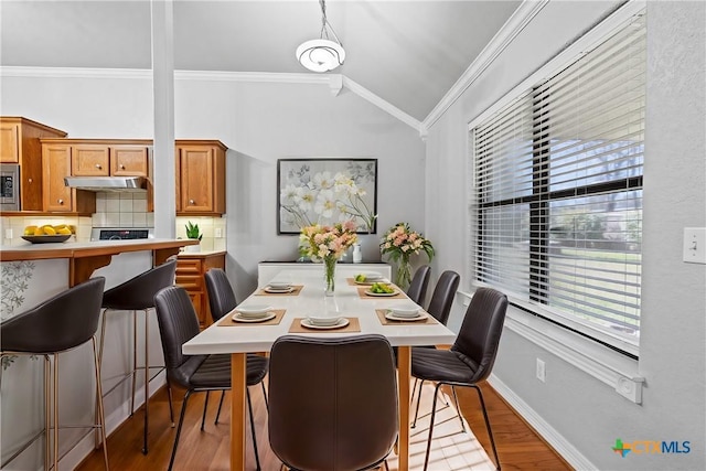 dining area with lofted ceiling, baseboards, wood finished floors, and crown molding