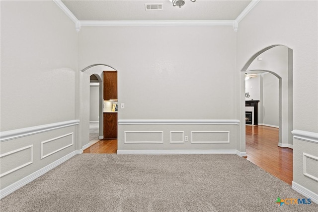 carpeted empty room with arched walkways, visible vents, and crown molding