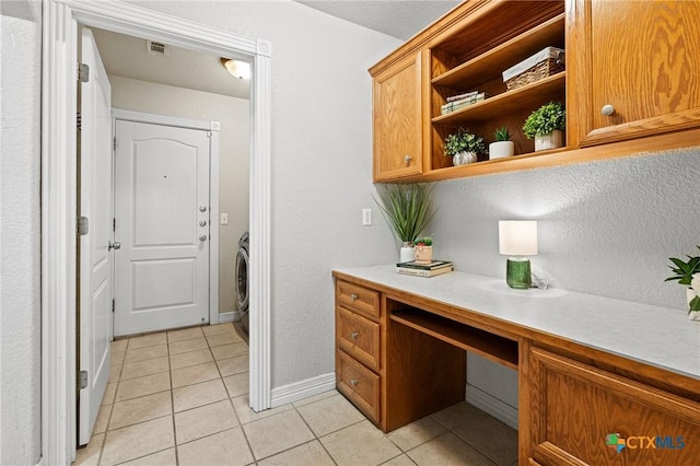 interior space with light tile patterned floors, visible vents, baseboards, built in study area, and washer / dryer