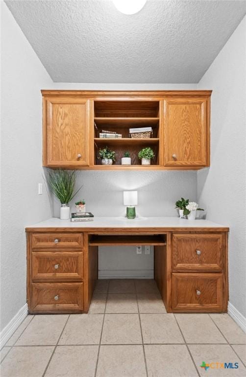 office featuring a textured ceiling, light tile patterned flooring, built in study area, and baseboards