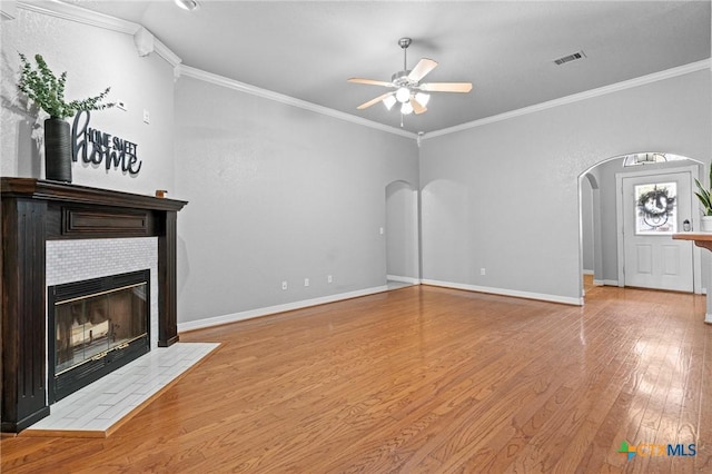 unfurnished living room with arched walkways, wood finished floors, visible vents, a ceiling fan, and a tiled fireplace