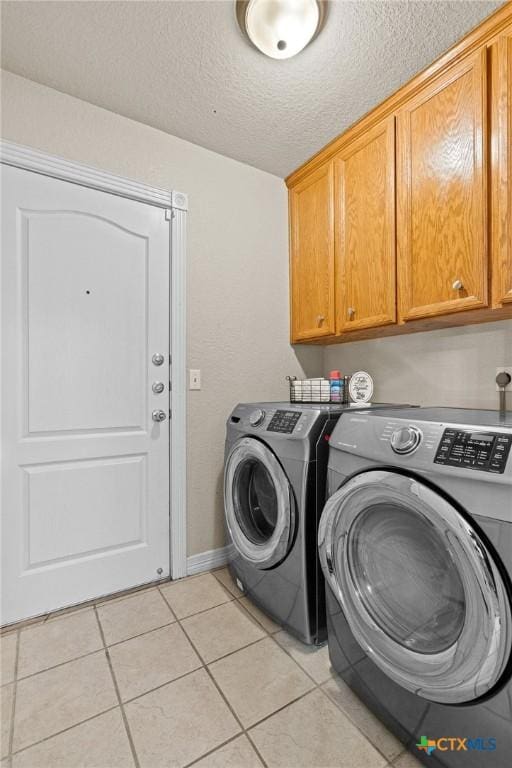 laundry area featuring a textured ceiling, separate washer and dryer, light tile patterned flooring, and cabinet space