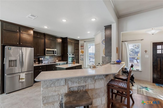 kitchen with backsplash, a kitchen breakfast bar, crown molding, appliances with stainless steel finishes, and dark brown cabinets