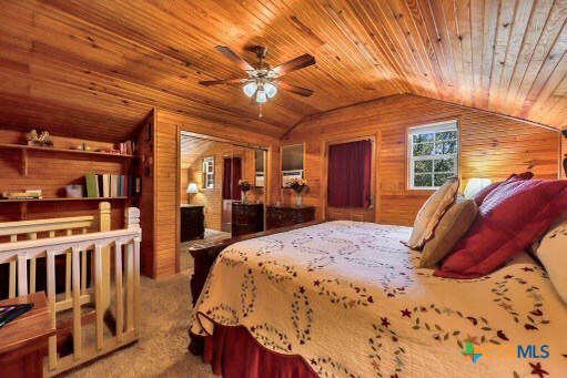 carpeted bedroom with wood walls, wood ceiling, vaulted ceiling, and ceiling fan