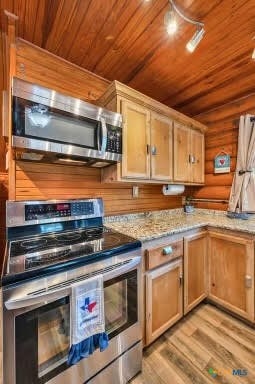 kitchen with stainless steel appliances, light stone counters, wood ceiling, wooden walls, and light wood-type flooring