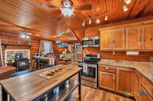 kitchen featuring stainless steel appliances, wooden ceiling, a wood stove, log walls, and light wood-type flooring