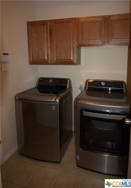 laundry room featuring washing machine and dryer, cabinets, and light tile patterned floors