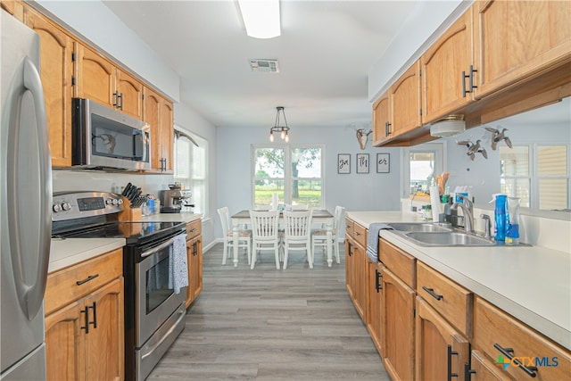 kitchen with pendant lighting, appliances with stainless steel finishes, sink, and light hardwood / wood-style floors