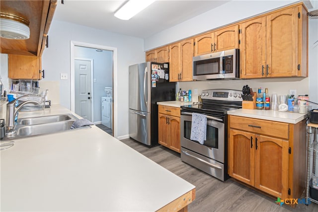 kitchen with stainless steel appliances, washer / dryer, sink, and dark wood-type flooring