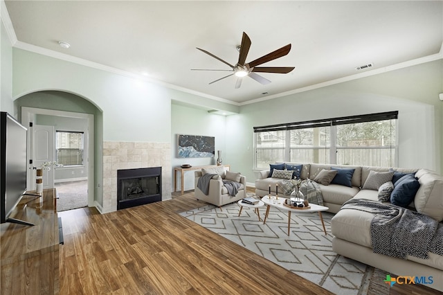 living area featuring visible vents, a ceiling fan, ornamental molding, wood finished floors, and a fireplace