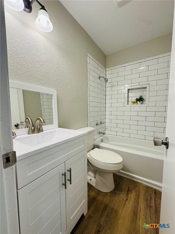 bathroom with a textured wall, toilet, shower / bathtub combination, wood finished floors, and vanity