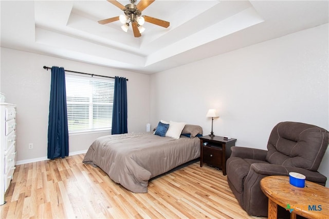 bedroom featuring ceiling fan, a raised ceiling, and light wood-type flooring