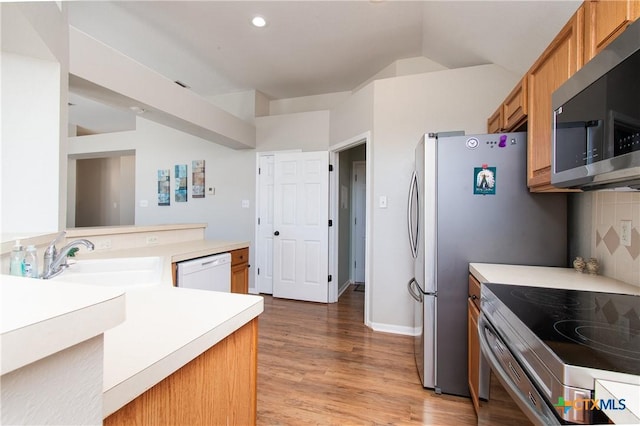 kitchen with sink, stainless steel appliances, light hardwood / wood-style flooring, kitchen peninsula, and vaulted ceiling