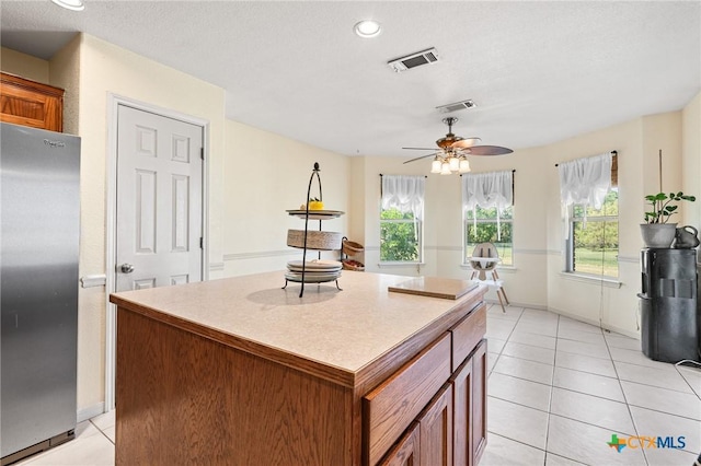 3197 Robin Ln, Kempner, TX 76539 - kitchen with freestanding refrigerator, light tile patterned floors, a kitchen island, ceiling fan, and brown cabinetry