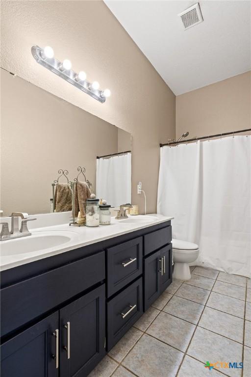 3197 Robin Ln, Kempner, TX 76539 - full bath with double vanity, tile patterned flooring, toilet, a shower with shower curtain, and vaulted ceiling