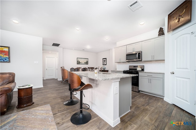 kitchen with stainless steel appliances, a kitchen bar, an island with sink, dark wood-type flooring, and gray cabinetry