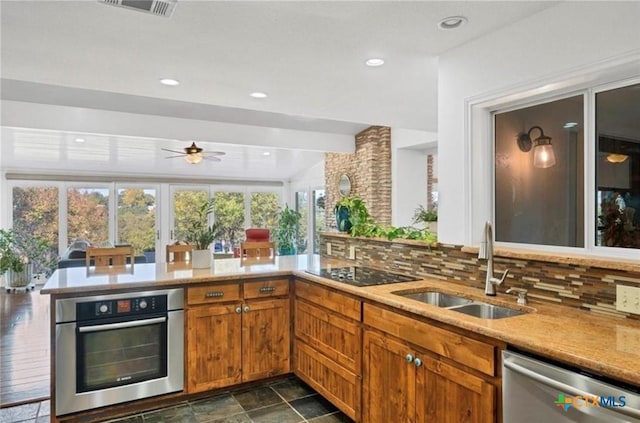 kitchen featuring sink, kitchen peninsula, ceiling fan, stainless steel appliances, and backsplash