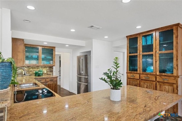 kitchen featuring sink, black electric stovetop, light stone countertops, decorative backsplash, and high end refrigerator