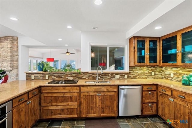 kitchen featuring brown cabinetry, stainless steel dishwasher, light stone countertops, and a sink